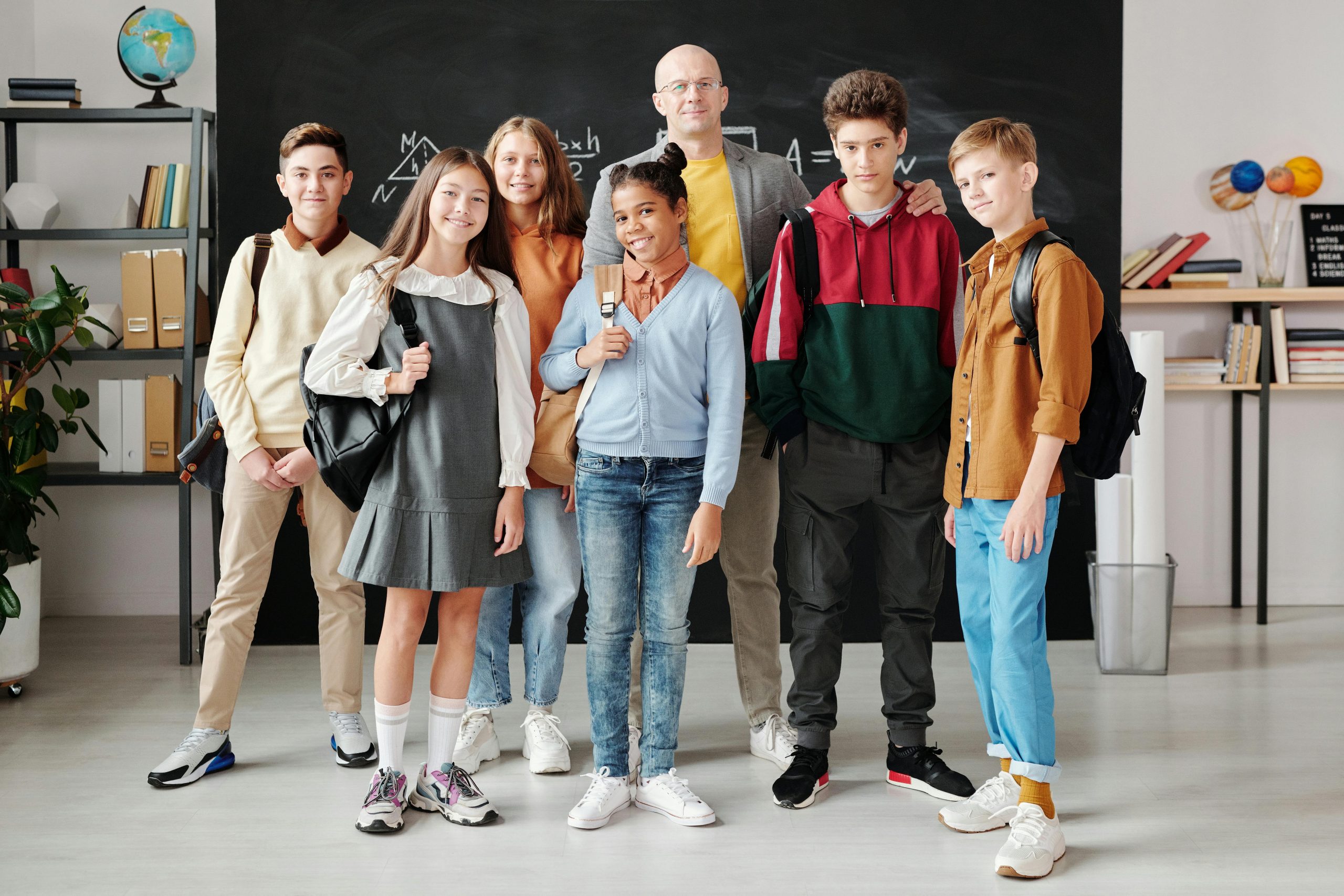 Group of diverse teenagers posing with their teacher in a modern classroom.